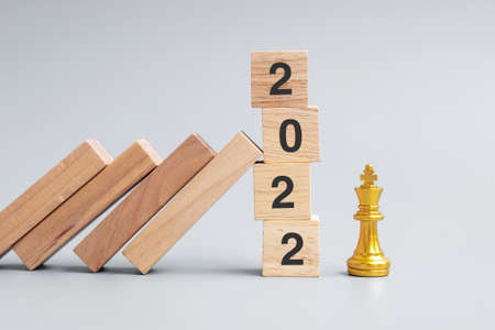 wooden Dominoes falling against 2022 stop blocks with golden Chess King figure. Business, Risk Management, Solution, economic, Insurance and New Year conceptの写真素材