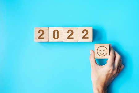 hand holding Smile face block with 2022 text on blue background. Satisfaction, feedback, Review and New Year conceptsの写真素材