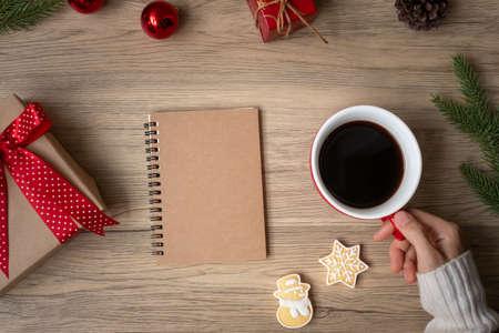 Woman hand holding black coffee cup with blank notebook and Christmas cookies on table. Xmas, Happy New Year, Goals, Resolution, To do list, Strategy and Plan conceptの写真素材