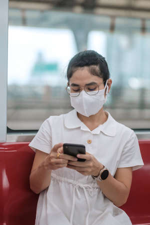 woman using smartphone during wearing protective face mask in train. public transportation,...