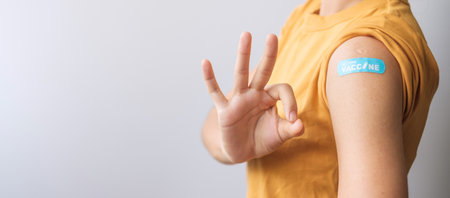 woman showing OK sign with bandage after receiving covid 19 vaccine. Vaccination, herd immunity,...