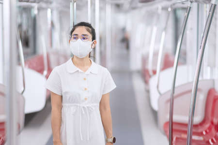 woman wearing Medical face mask and listening music by earphones in train. public transportation and safety under covid-19 pandemicの写真素材