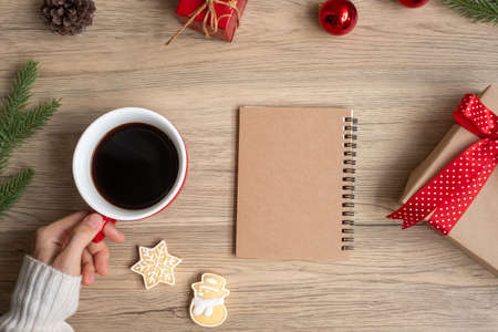 Woman hand holding black coffee cup with blank notebook and Christmas cookies on table. Xmas, Happy New Year, Goals, Resolution, To do list, Strategy and Plan conceptの写真素材
