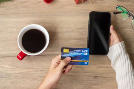 Hand holding credit card for online shopping on smartphone during drinking coffee. Merry Christmas eve, December, seasonal, Black Friday sale, New Year and holiday conceptの写真素材