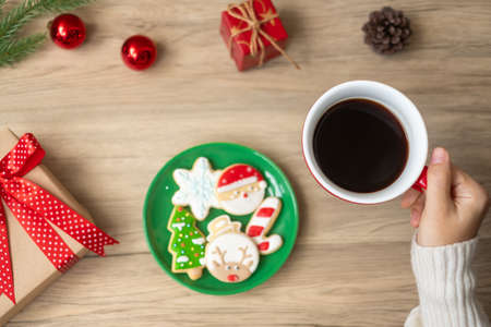 Merry Christmas with woman hand holding coffee cup and homemade cookie on table. Xmas eve, party, holiday and happy New Year conceptの写真素材