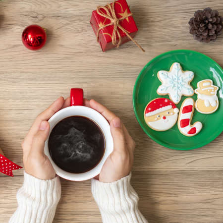 Merry Christmas with woman hand holding coffee cup and homemade cookie on table. Xmas eve, party, holiday and happy New Year conceptの写真素材
