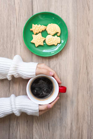 Merry Christmas with woman hand holding coffee cup and homemade cookie on table. Xmas eve, party, holiday and happy New Year conceptの写真素材