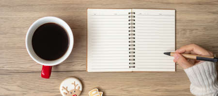Woman hand writing on notebook with black coffee cup and Christmas cookies on table. Xmas, Happy New Year, Goals, Resolution, To do list, Strategy and Plan conceptの写真素材