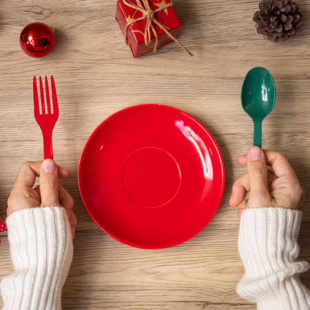 Merry Christmas with woman hand holding plate, fork and spoon on wood table background. Xmas, party and happy New Year conceptの写真素材