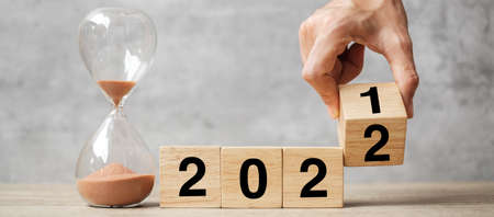 hand flipping block 2021 to 2022 text with hourglass on table. Resolution, time, plan, goal, motivation, reboot, countdown  and New Year holiday conceptsの写真素材