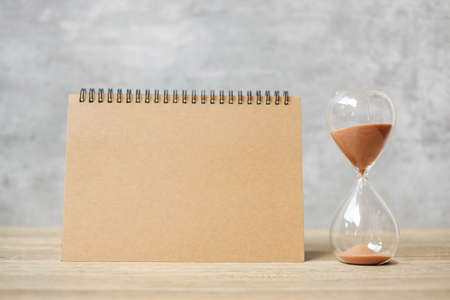 Hourglass with Blank notebook on table, Sand flowing through the bulb of Sandglass measuring the passing. countdown, deadline, Life time and Retirement conceptの写真素材