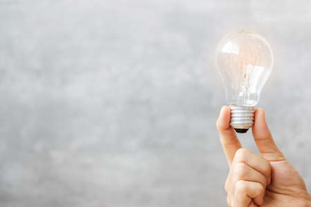 Hand holding light bulb on wall background. New Ideas, Creative, Innovation, Imagination, inspiration, Resolution, Strategy and goal conceptの写真素材