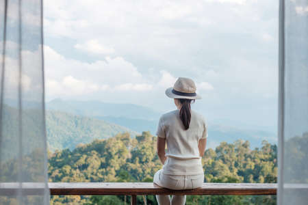 Happy tourist woman relaxing and looking mountain view at countryside home or homestay in the morning. Vacation, blogger, SoloTravel, journey, trip and relaxing conceptの写真素材