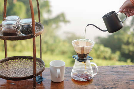 Hand pouring Hot water during brewing arabica coffee by Vintage coffee drip equipment on wooden table in the morning with mountain and nature backgroundの写真素材