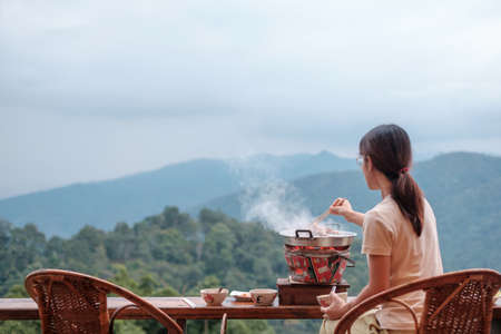 Woman grill Pork or meat with vegetables and soup on the hot pan against mountain view background, Traditional Thai BBQ style is famous in Thailandの写真素材