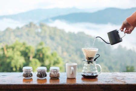 Hand pouring Hot water during brewing arabica coffee by Vintage coffee drip equipment on wooden table in the morning with mountain and nature backgroundの写真素材