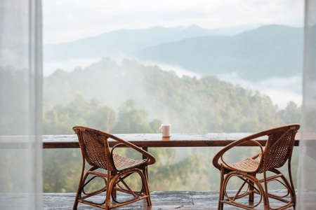 White mug of hot coffee or tea on wooden table in the morning with mountain and nature backgroundの写真素材