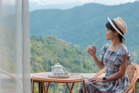 woman drinking tea and looking mountain view, young blogger stay at countryside homestay in the morning.Travel, vacation, journey, trip and relaxing conceptの写真素材