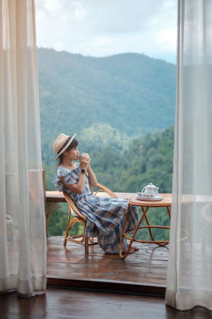 woman drinking tea and looking mountain view, young blogger stay at countryside homestay in the morning.Travel, vacation, journey, trip and relaxing conceptの写真素材