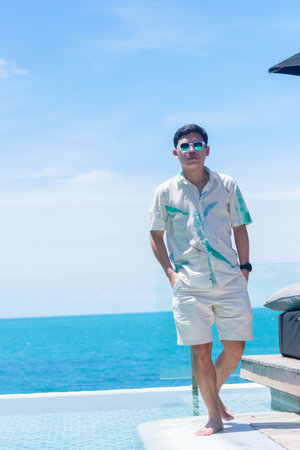 Happy man walking near infinity pool at luxury hotel against ocean front. young male enjoy in tropical resort. Relaxing, summer,  travel, holiday, vacation and weekend conceptの写真素材