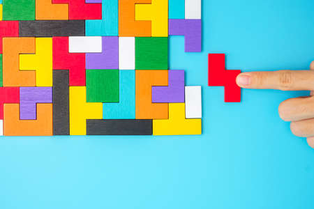 Hand connecting colorful wood puzzle pieces on blue background, geometric shape block. Concepts of logical thinking, Conundrum, solutions, rational, strategy, world logic day and Educationの写真素材