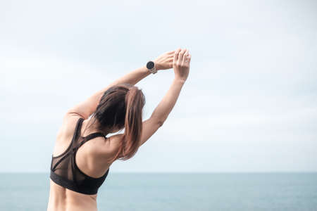 Young fitness female in sportswear stretching body against ocean view, healthy woman exercise in...