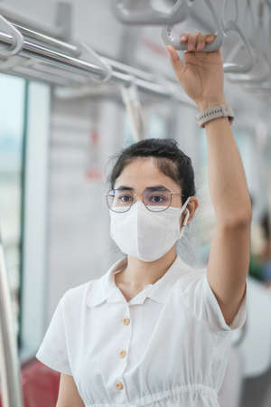 woman with Medical face mask, Hand holding handle and listening music by earphones in train.の写真素材