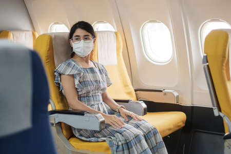 woman wearing protective face mask sitting in airplaneの写真素材