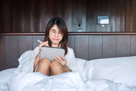 Happy woman using tablet for social media, young female watching movies on computer pad on bed at home. technology, network, online shopping, e commerce, lifestyle and digital communication conceptの写真素材