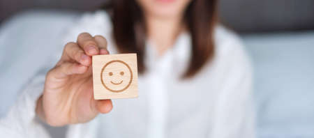 Happy Woman holding smile emotion face block. Customer choose Emoticon for user reviews. Service rating, mental health, positive thinking, satisfaction, evaluation and feedback conceptの写真素材