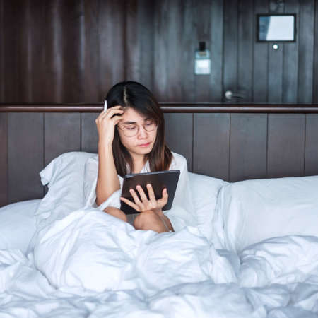 Happy woman using tablet for social media, young female watching movies on computer pad on bed at home. technology, network, online shopping, e commerce, lifestyle and digital communication conceptの写真素材
