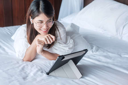Happy woman using tablet for social media, young female watching movies on computer pad on bed at home. technology, network, online shopping, e commerce, lifestyle and digital communication conceptの写真素材
