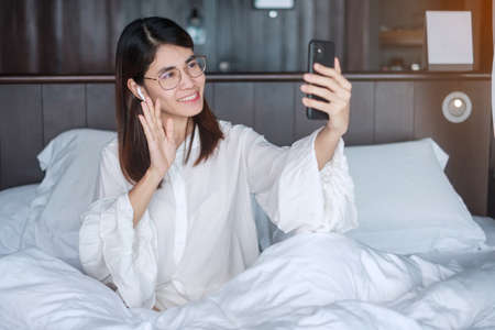 Happy woman using smart phone for video call, female meeting  online by mobile phone on bed. technology, network, work from home, lifestyle and digital communication conceptの写真素材