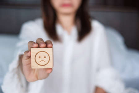 Woman holding angry emotion face block. Customer choose Emoticon for user reviews. Service rating, mental health, positive thinking, satisfaction, evaluation and feedback conceptの写真素材