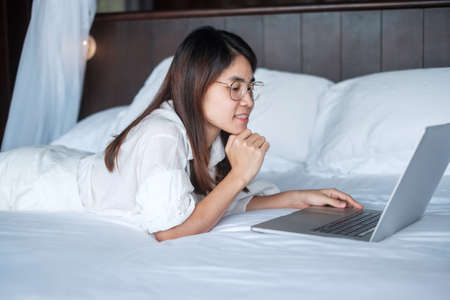 Happy woman using laptop for work, female meeting  online by computer notebook on bed. technology, network, work from home, lifestyle and digital communication conceptの写真素材