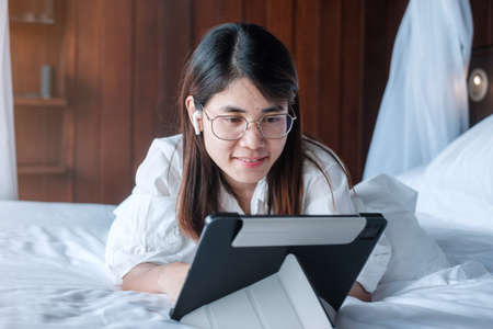 Happy woman using tablet for social media, young female watching movies on computer pad on bed at home. technology, network, online shopping, e commerce, lifestyle and digital communication conceptの写真素材