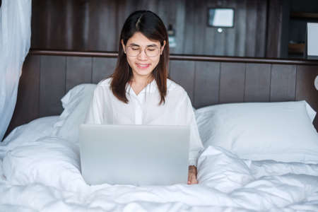 Happy woman using laptop for work, female meeting  online by computer notebook on bed. technology, network, work from home, lifestyle and digital communication conceptの写真素材