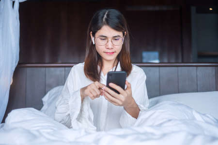 Happy woman using smart phone for video call, female meeting  online by mobile phone on bed. technology, network, work from home, lifestyle and digital communication conceptの写真素材