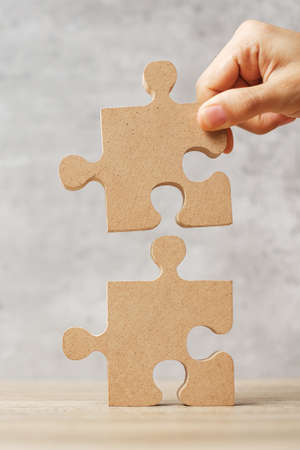 Man connecting couple puzzle piece, wood jigsaw on table. Business solutions, mission, success, goals and strategy conceptsの写真素材