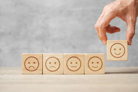 Man hand holding emotion face block. Customer choose Emoticon for user reviews. Service rating, ranking, customer review, satisfaction, mood, evaluation and feedback conceptの写真素材