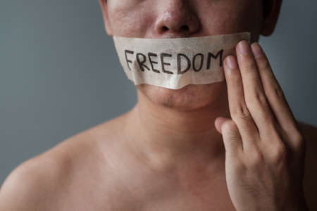 Man show three fingers  with mouth sealed in adhesive tape with Freedom message. Free of speech, Human rights, Protest dictatorship, democracy, liberty, equality and fraternity conceptsの写真素材