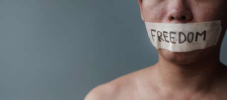 Man with mouth sealed in adhesive tape with Freedom message. Free of speech, freedom of press, Human rights, Protest dictatorship, democracy, liberty, equality and fraternity conceptsの写真素材