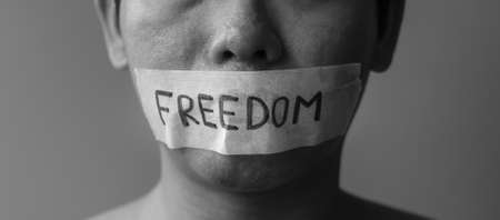 Man with mouth sealed in adhesive tape with Freedom message. Free of speech, freedom of press, Human rights, Protest dictatorship, democracy, liberty, equality and fraternity conceptsの写真素材