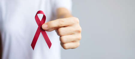 hand holding Burgundy Red Ribbon for March multiple myeloma Cancer and December World Aids Day Awareness month. Healthcare and world cancer day conceptの写真素材