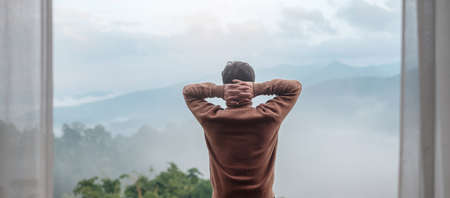 happy tourist man relaxing and looking mountain view at countryside home or homestay in the morning. Vacation, blogger, SoloTravel, journey, trip and relaxing conceptの写真素材
