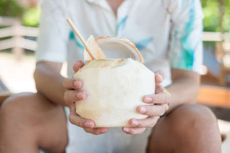 Man holding fresh coconut juice during drinking on tropical beach. Summer, relaxing and vacation conceptsの写真素材