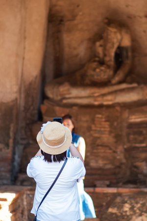 Happy tourist woman in white dress taking Photo by mobile smartphone, during visiting in Wat Chaiwatthanaram temple in Ayutthaya Historical Park, summer, solo, Asia and Thailand travel conceptの写真素材