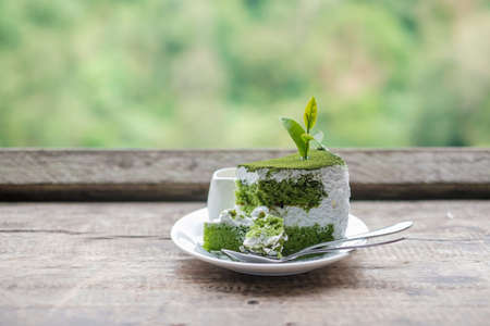 Green tea cake with young bud tea leaf on wooden table against tea garden backgroundの写真素材