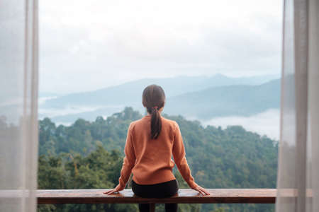 Happy woman relaxing and looking mountain view at countryside home or homestay in the morning. Vacation, blogger, SoloTravel, journey, trip and relaxing conceptの写真素材