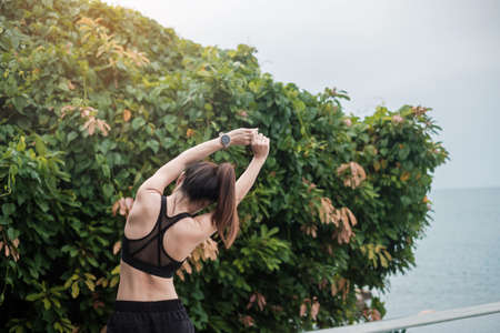 Young fitness female in sportswear stretching body against ocean view, healthy woman exercise in...